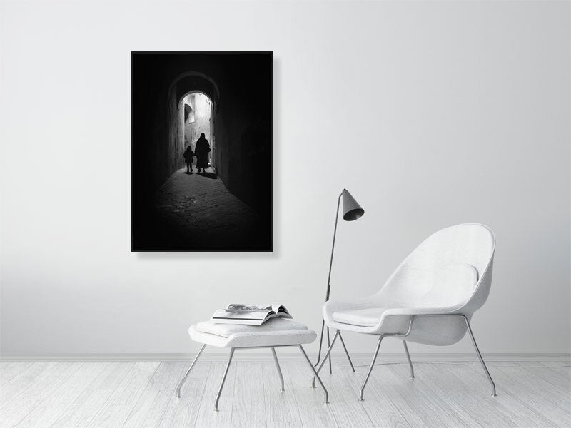 Monochrome photograph of a woman and child walking through a narrow alley under soft daylight. The scene evokes quiet observation and documentary calm — a defining image for the visual tone of Dustlight Archive.