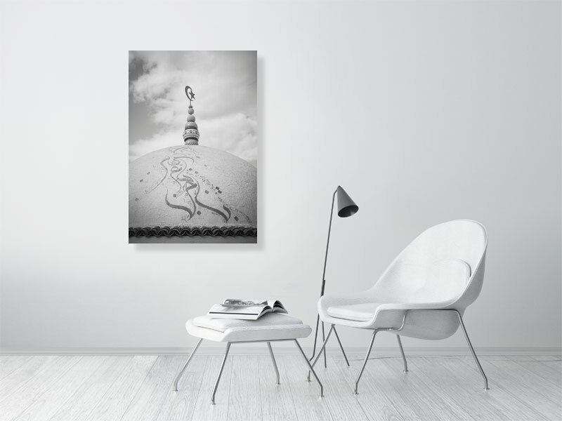 Black and white photograph of a domed rooftop adorned with Arabic calligraphy and topped by a crescent and star finial. The textured surface and cloudy sky create a calm, spiritual atmosphere emphasizing form and symbolism.