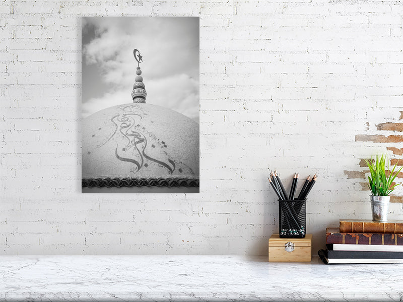 Black and white photograph of a domed rooftop adorned with Arabic calligraphy and topped by a crescent and star finial. The textured surface and cloudy sky create a calm, spiritual atmosphere emphasizing form and symbolism.
