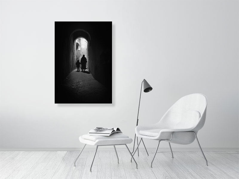 Monochrome photograph of a woman and child walking through a narrow alley under soft daylight. The scene evokes quiet observation and documentary calm — a defining image for the visual tone of Dustlight Archive.