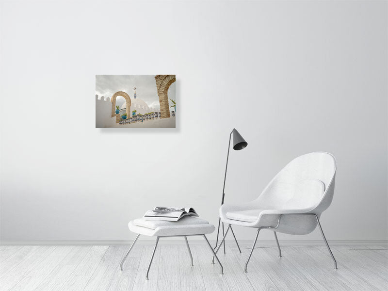 Photograph of a white dome with a crescent and star finial framed by stone arches and blue ceramic pots on a terrace in Tunisia. The scene captures calm Mediterranean architecture under a cloudy sky, emphasizing geometry, texture, and soft light.