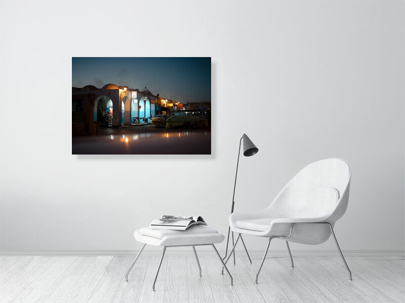 Evening photograph of a quiet market street illuminated by warm streetlights during the blue hour. Arched facades, parked cars, and covered stalls create a cinematic atmosphere, blending calm light with deep twilight tones.